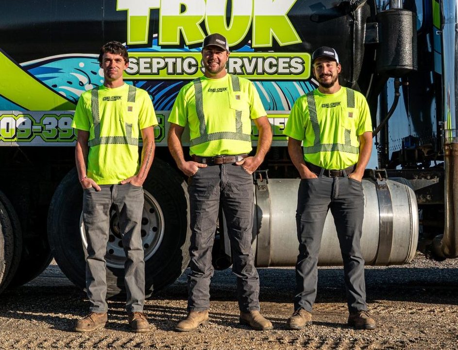 Three men in safety vests by a septic truck
